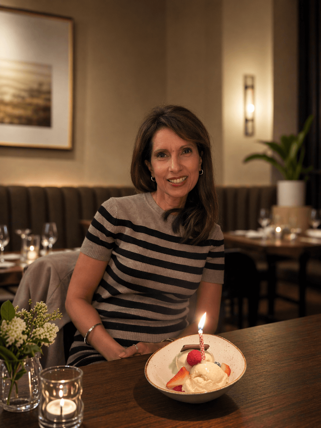 Smiling woman in a striped top at a restaurant table with a lit birthday candle.